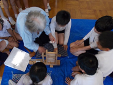 綿の種取りをするための道具を児童が見せてもらっている。