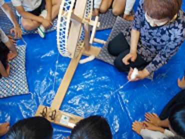 糸を紡ぐための道具を使う様子を児童が見せてもらっている。