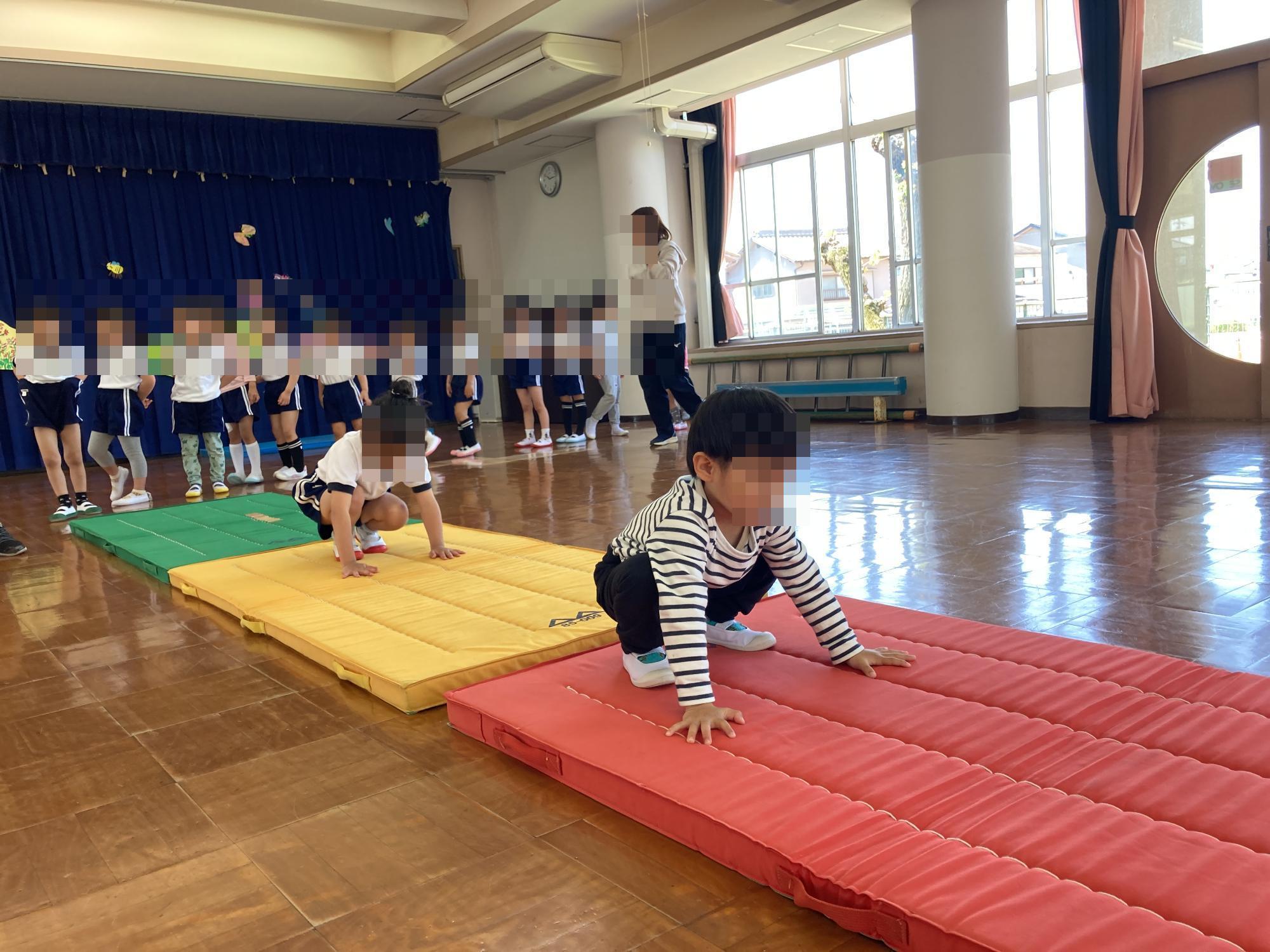 マットの上でかえる飛びをする幼児
