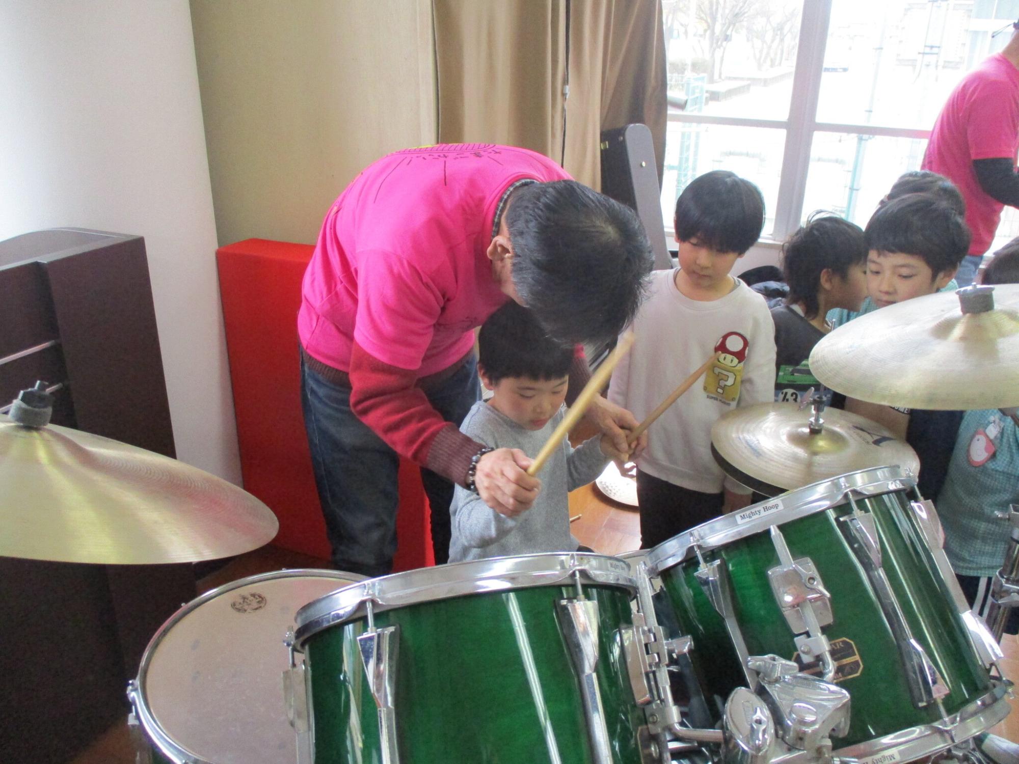ドラムを教えてもらいながら演奏する幼児