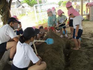 中学生と一緒に砂場で大きな山を作っている