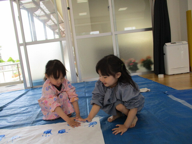 手に絵の具をつけた園児2人が向かい合い、スタンプ遊びをしている
