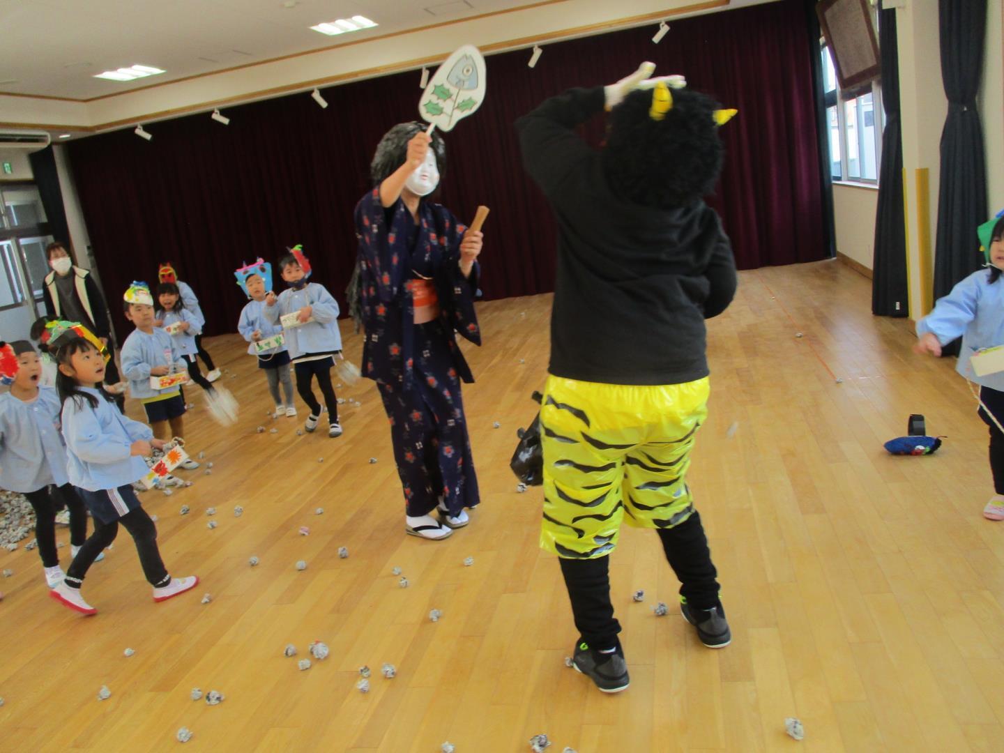 子ども達が、やってきた鬼に新聞で作った豆を投げ、立ち向かっている様子。