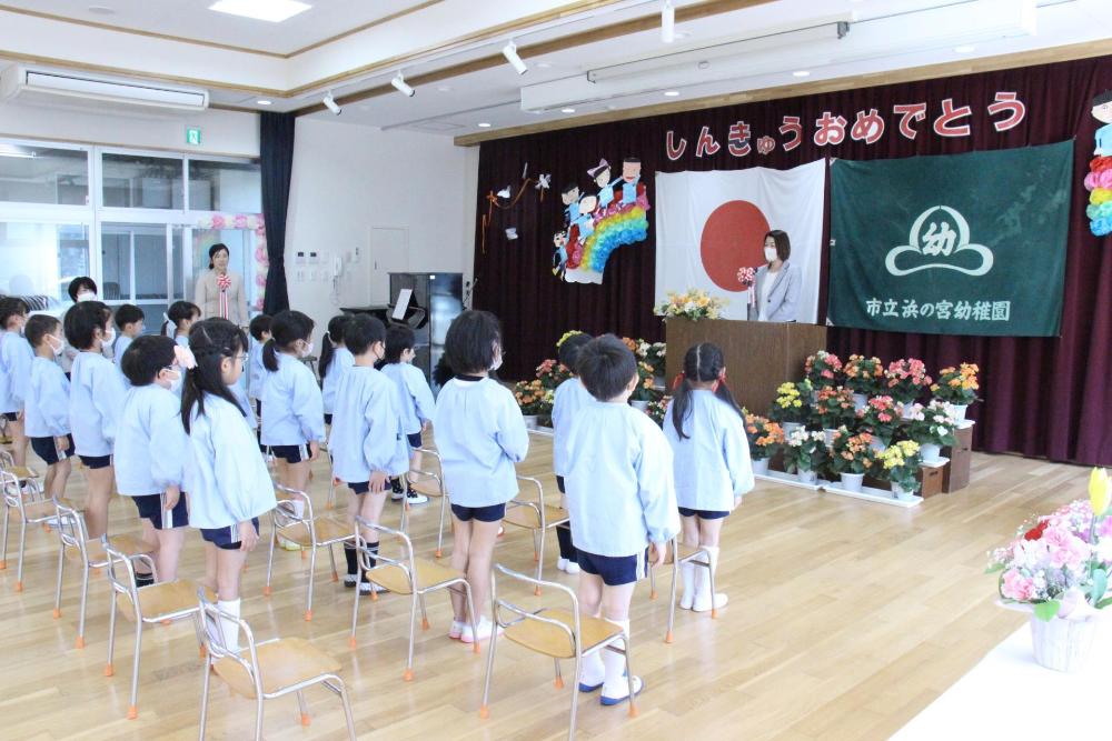 園児が遊戯室で園長先生の話を聞いているところ