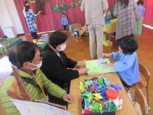 幼児が祖父母と紙相撲を楽しんでいる様子