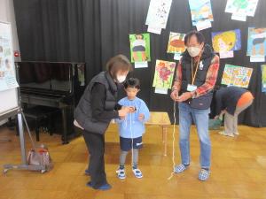 幼児が祖父母にコマの巻き方を教えてもらっている様子