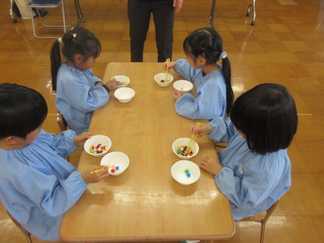 幼児が綿やマカロニ、豆を箸でつまんでいる様子