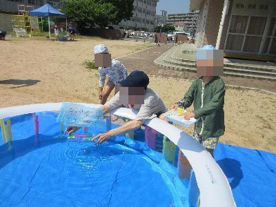作った船をプールに浮かべているお父さんとこどもの様子。