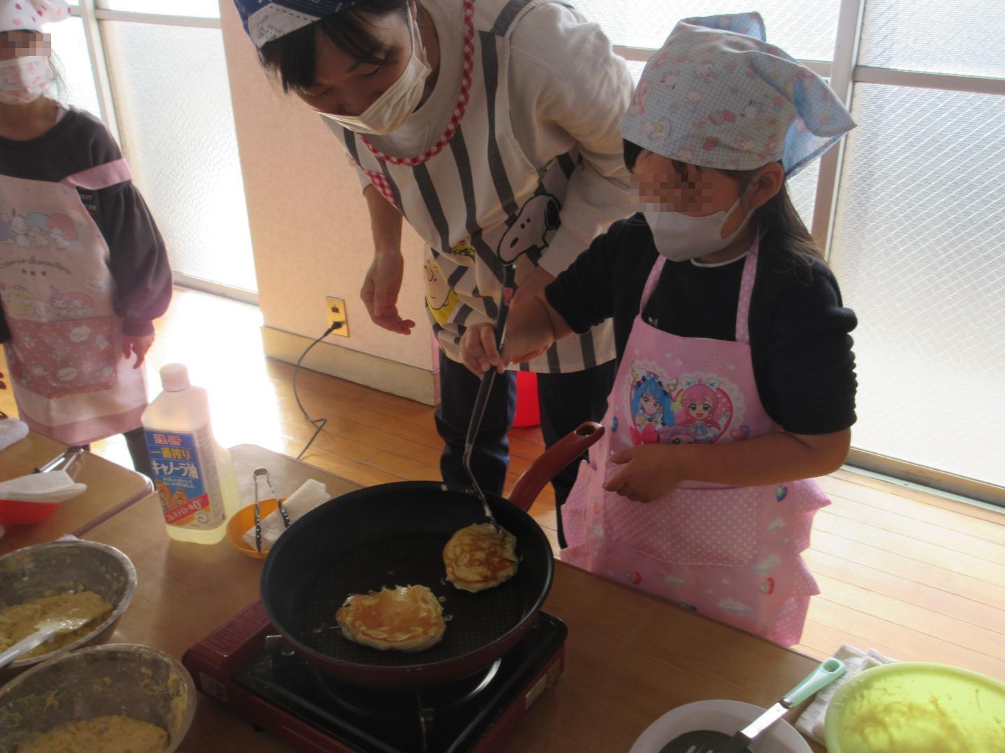 教師と一緒においもケーキをフライパンで焼く幼児