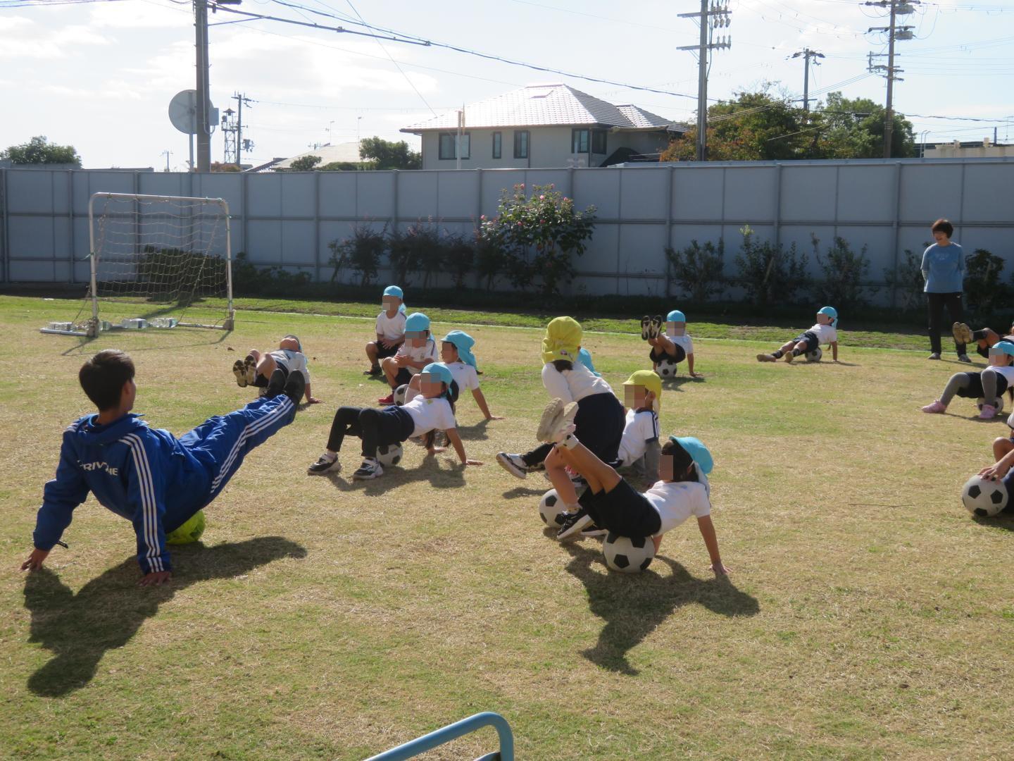 サッカーボールの上でV字バランスをする園児