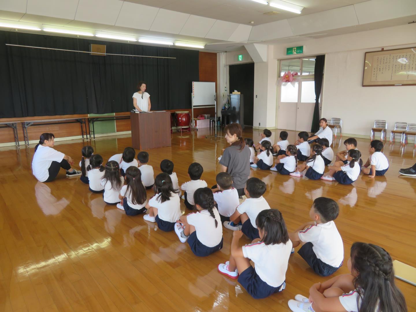 始業式で園長先生の話を聞いている幼児の写真です。