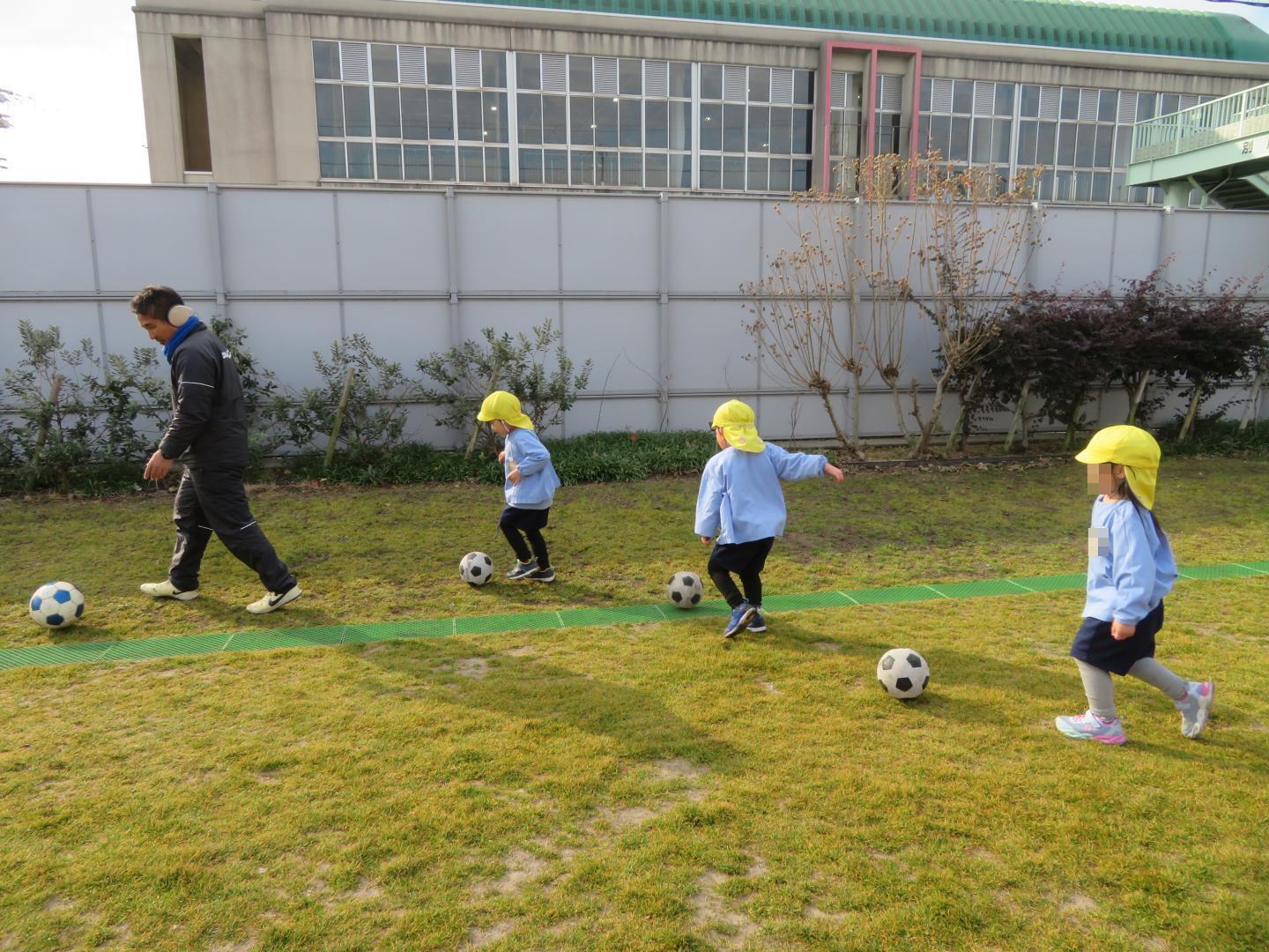 サッカーボールを蹴りながら進んで遊ぶ園児