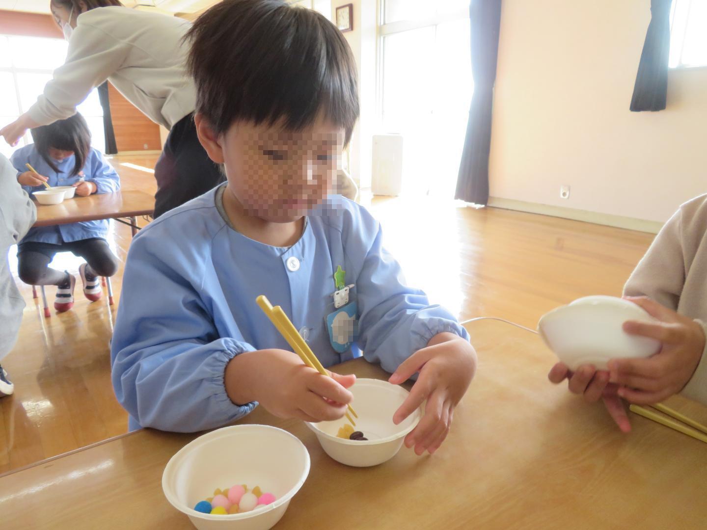 お箸でマカロニやフェルトボールを掴むことに挑戦している幼児