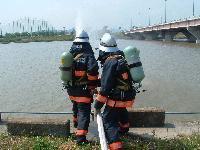 放水訓練をしている消防隊員の写真。放水先に大きな貯水池が確認できる