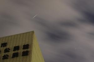 建物の上のほうに薄雲を通して見えるイリジウムフレアの光が短い線として見える写真