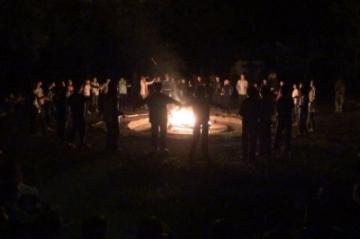 キャンプファイヤーで火の周りで人が輪になっている写真