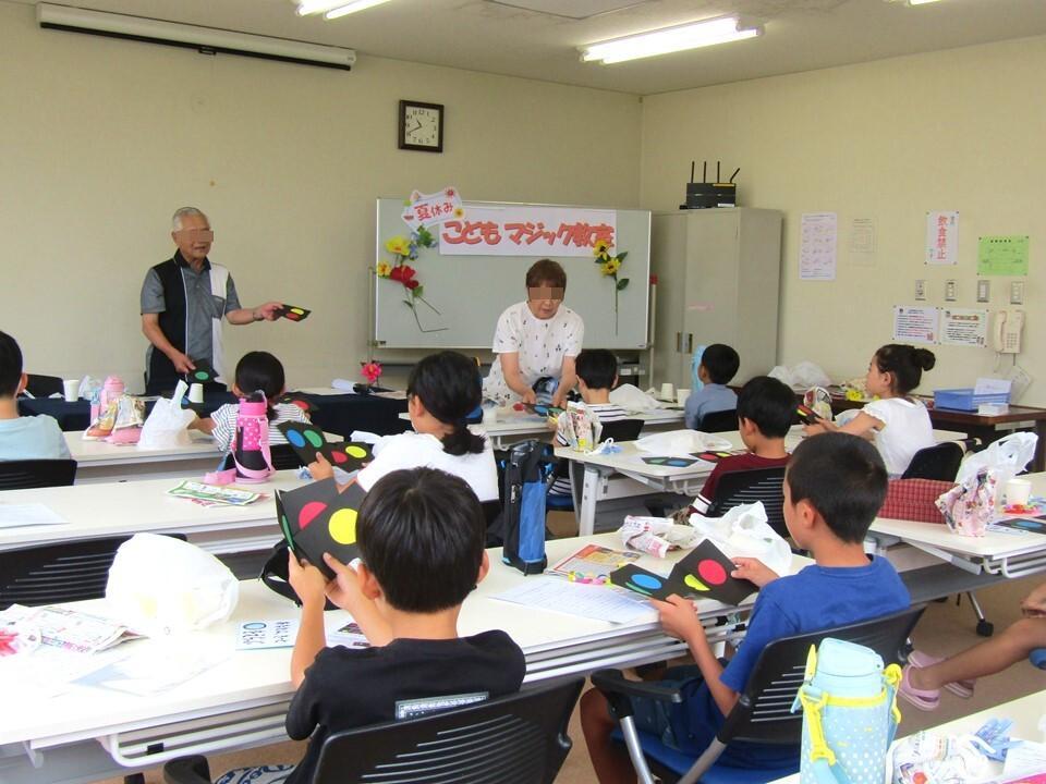 小学生が、先生から封筒を使ったマジックを教わっている様子