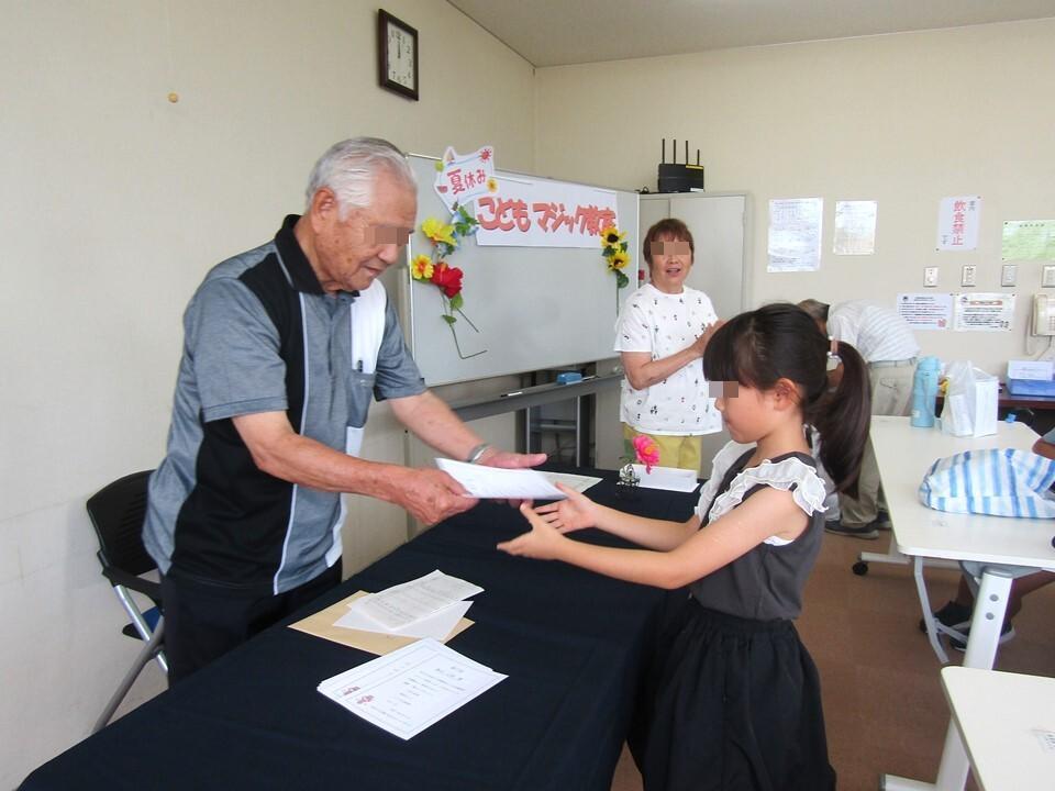 会の最後に、小学生が先生から修了証を受け取っている様子