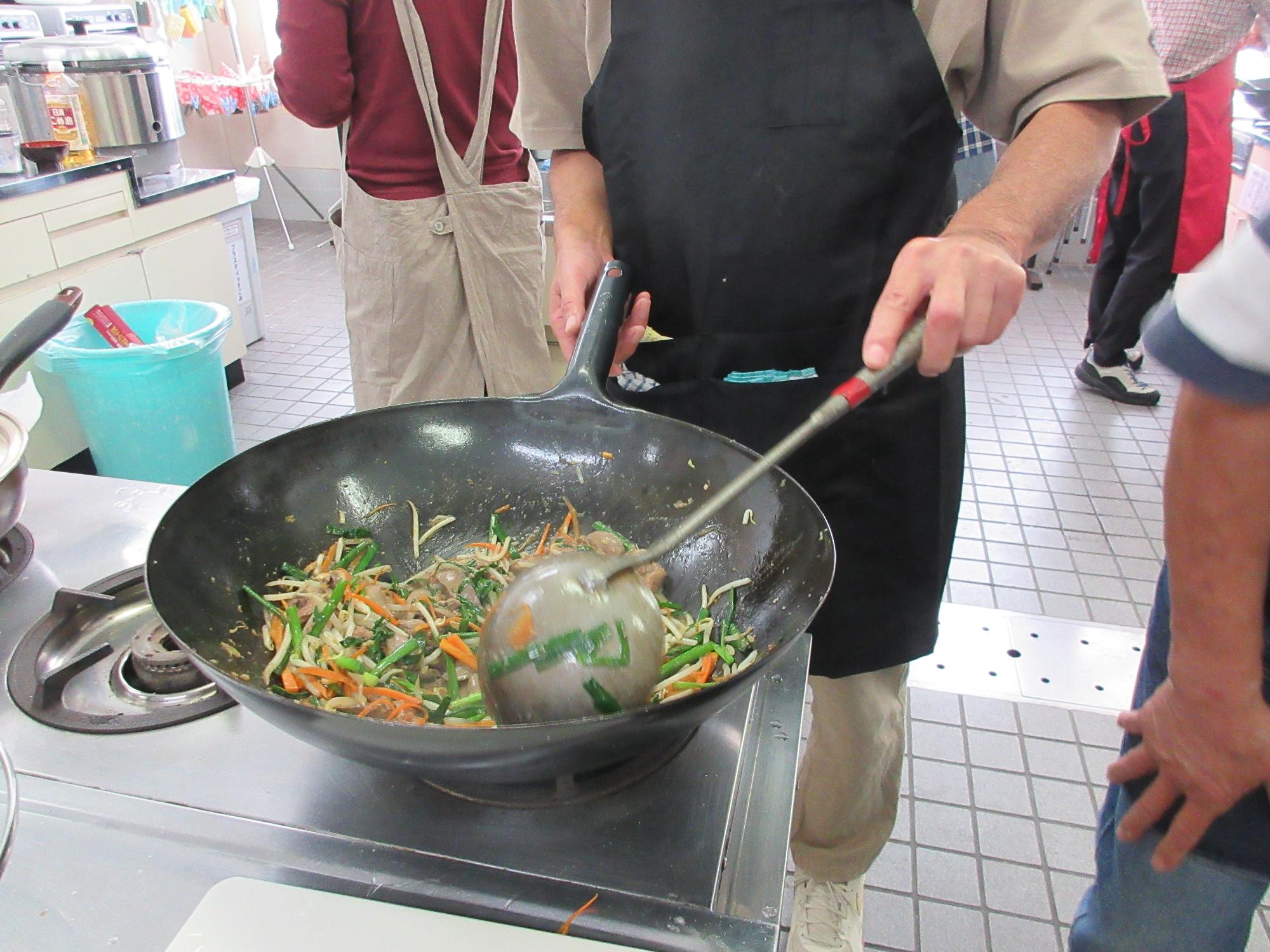 男性料理教室で、中華鍋を振って、レバニラを炒める様子です