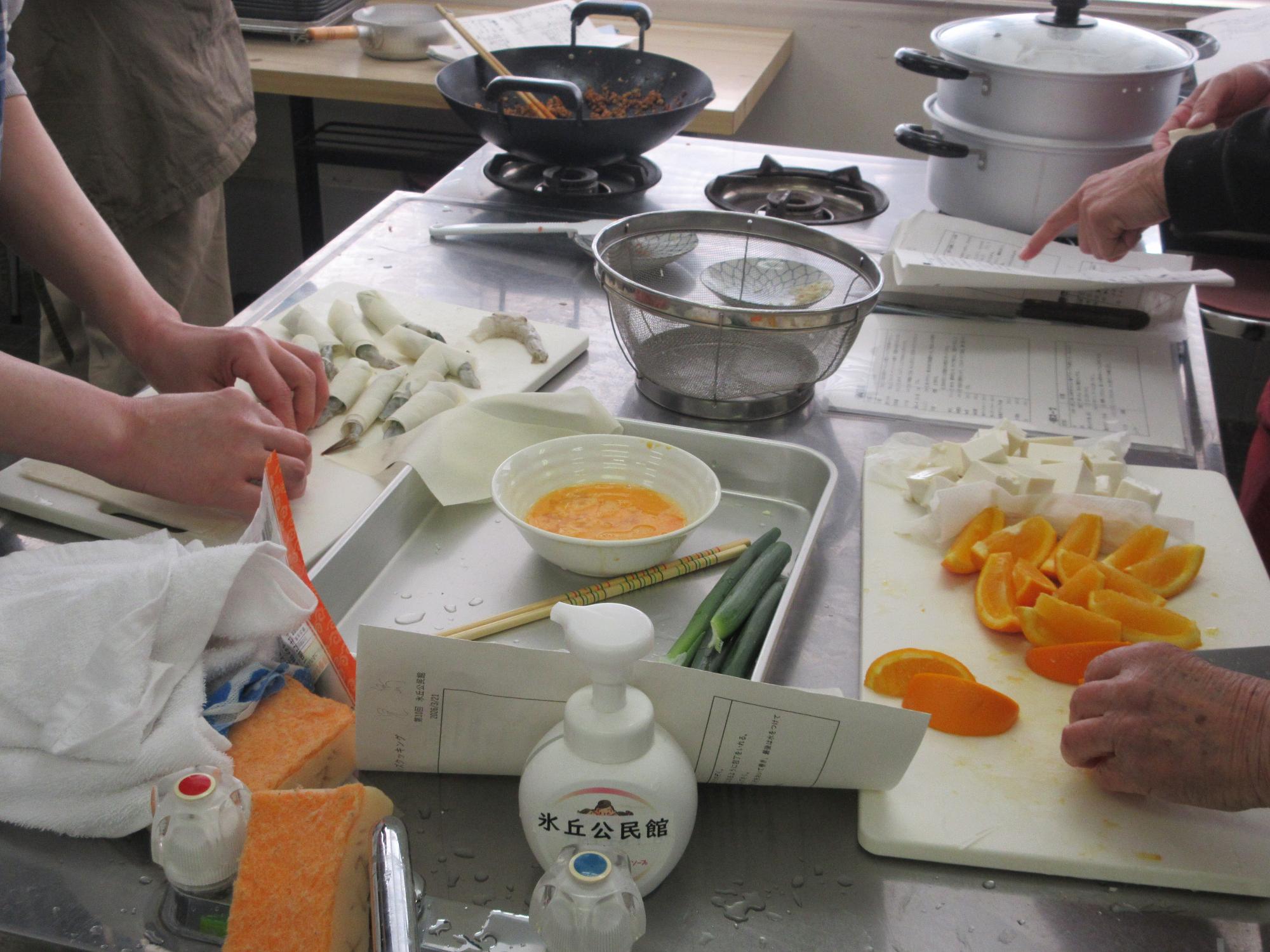 エビを春巻きの皮で巻くようすとオレンジを切るようす