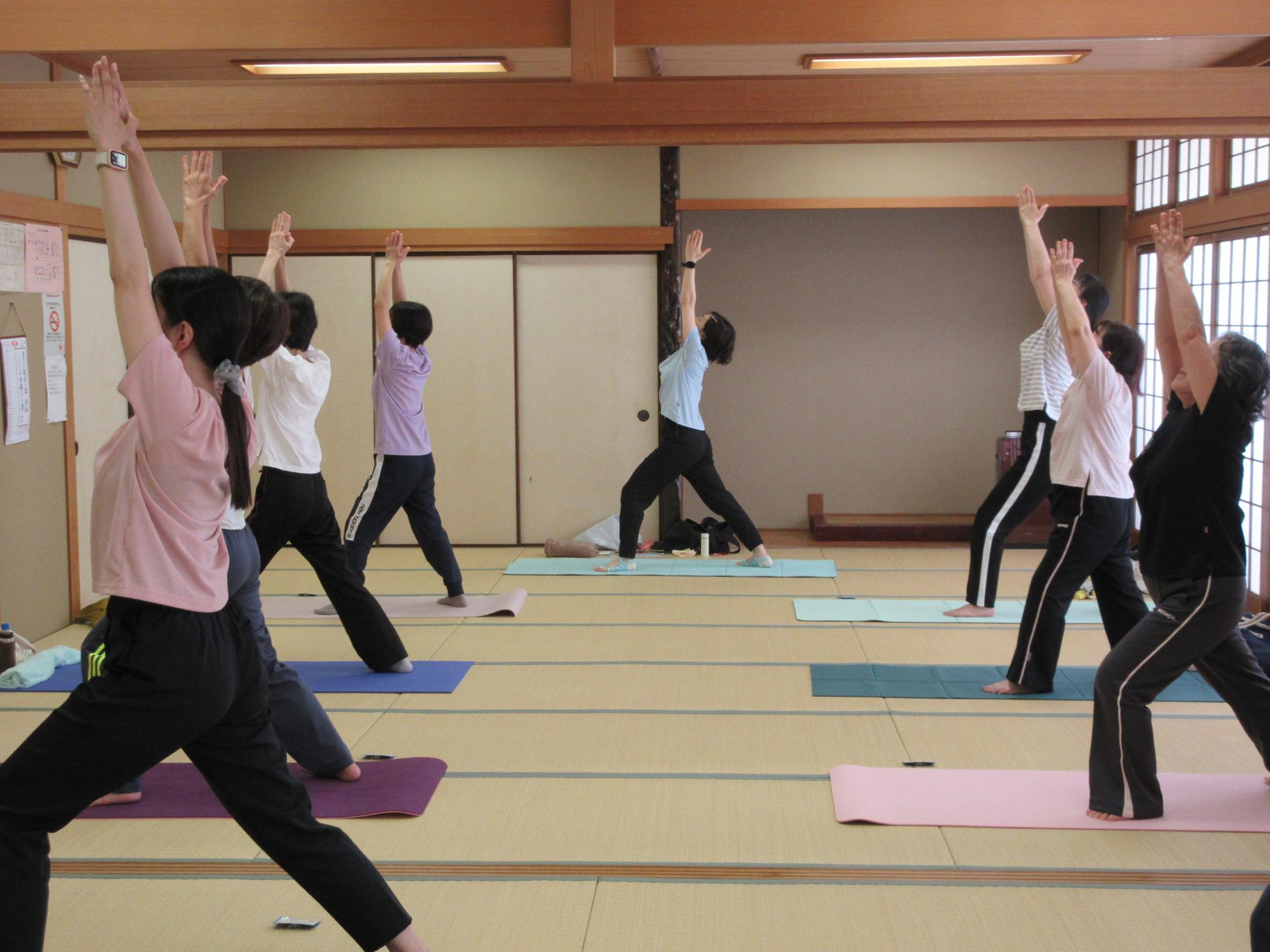 足を縦に開き、合わせた手を天井に向けて、身体を伸ばす様子