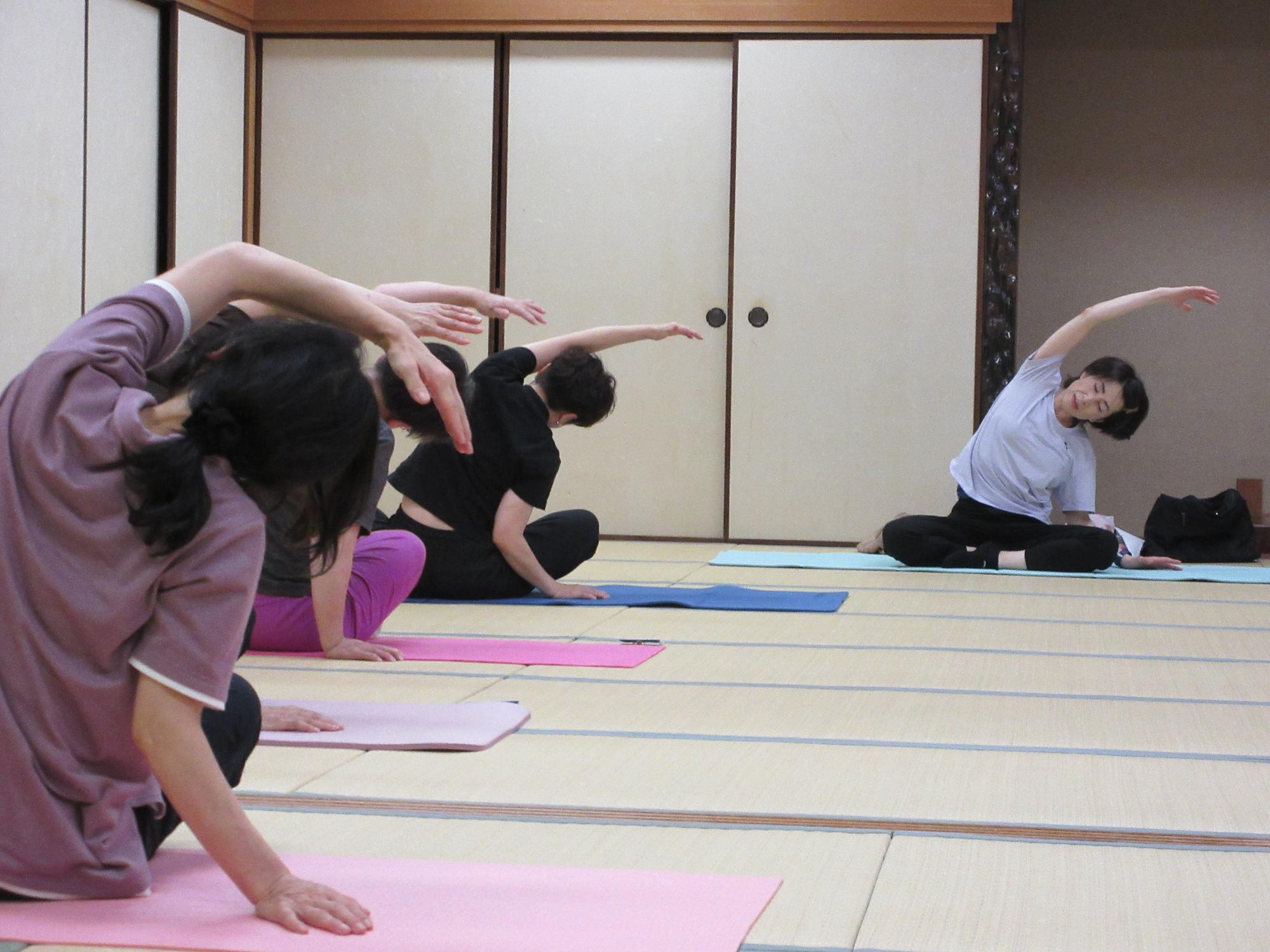 足を組んで座り、手を伸ばして身体を横に倒す様子