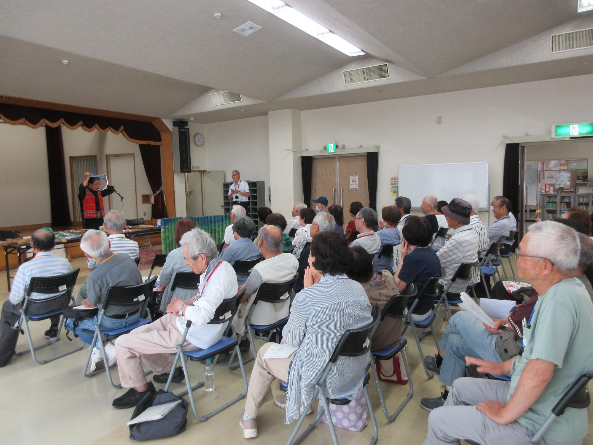 頭で鍵盤ハーモニカを演奏する講師とパフパフラッパを鳴らす学園長の様子
