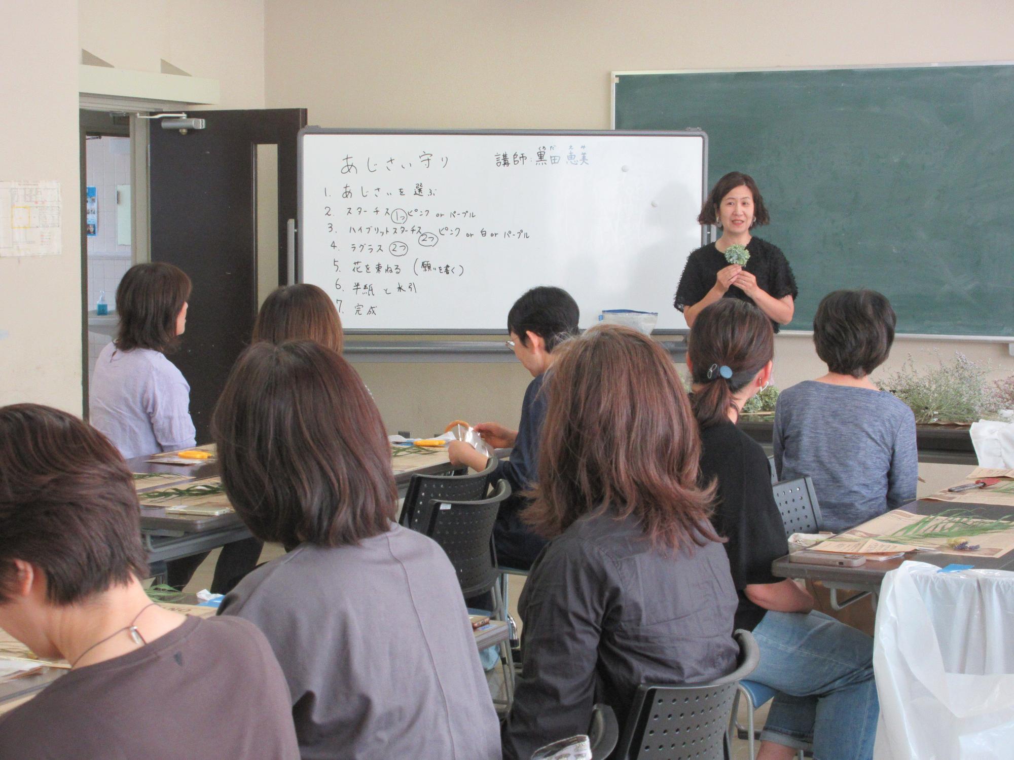 使用する花材の説明を聞く受講生と講師のようす