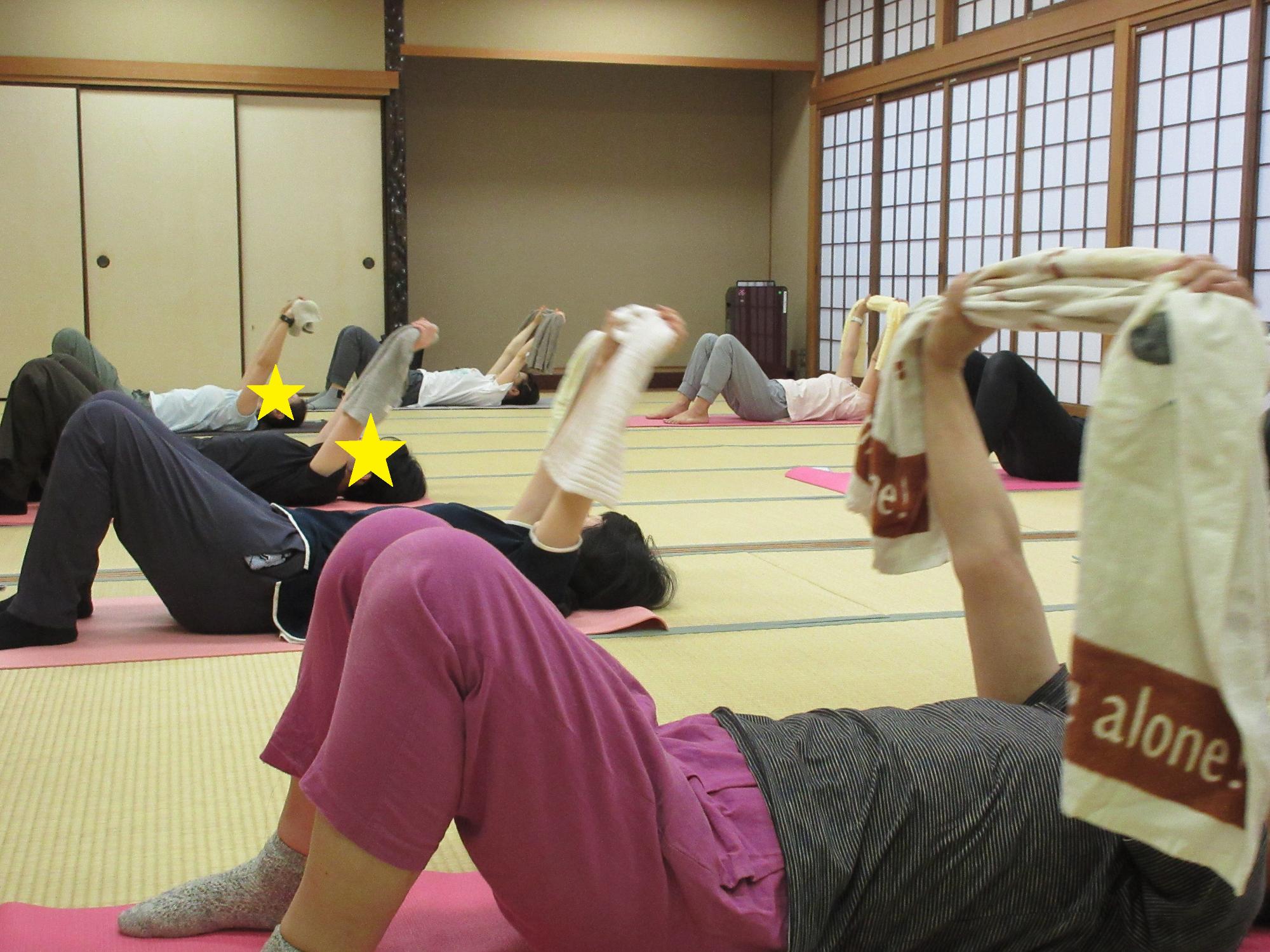 仰向けに寝転び両手にタオルを握って、頭上に腕を伸ばす様子