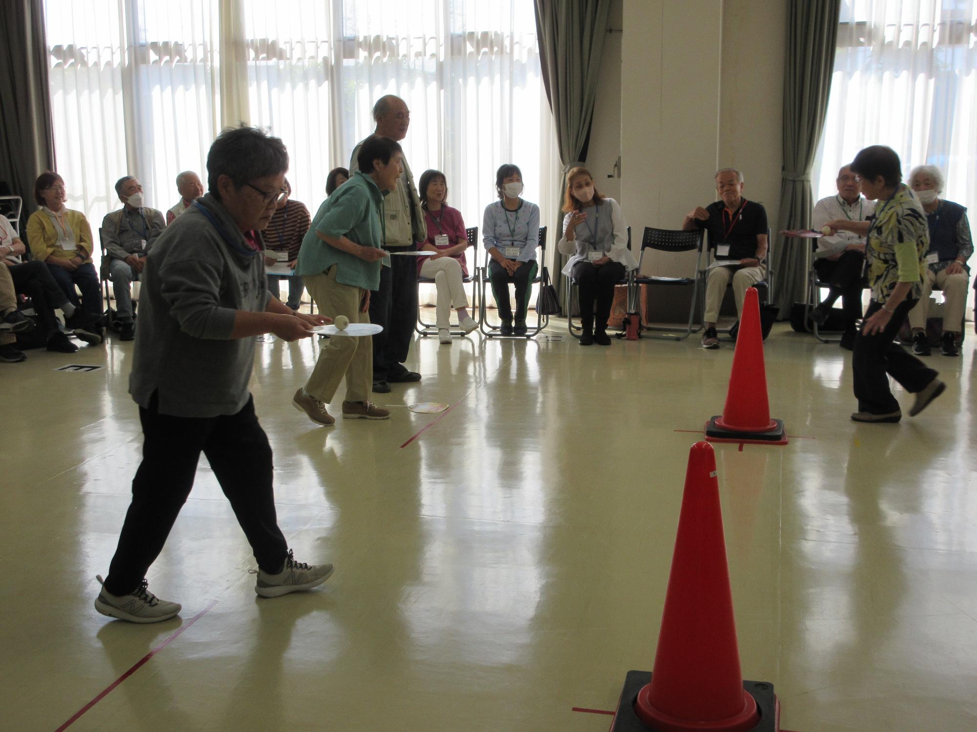 うちわにピン球を乗せて、障害物を避けながら歩くようす