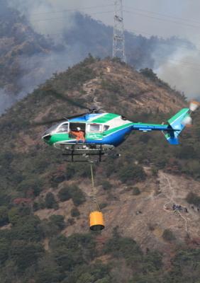 山々の上空をヘリが飛翔して消火活動を行っている写真