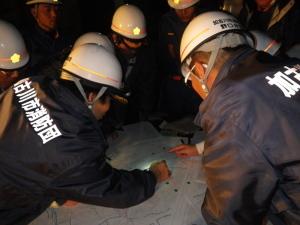訓練のため消防団員たちが地図を指で指し示し確認を行っている写真