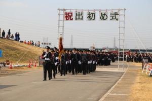 出初め式でプラカードや旗を持った先頭の団員に続いて行進をする消防団員たちの写真