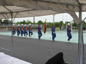 ポンプ操法大会の開会式で一列になり行進をする消防団員たちの写真